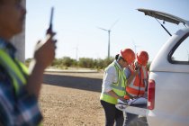 Engineers reviewing blueprints at truck at sunny wind turbine power plant — Stock Photo