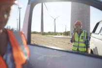 Smiling engineer using walkie-talkie at truck at sunny wind turbine power plant — Stock Photo