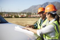 Engineers reviewing blueprints at truck at sunny power plant — Stock Photo
