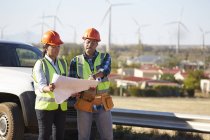 Ingenieure überprüfen Baupläne in der Nähe von Windkraftanlagen — Stockfoto