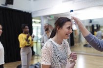 Friend holding water bottle to teenage girl?s forehead, cooling down in dance class studio — Stock Photo