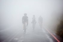 Присвячені чоловіки-велосипедисти їдуть по дощовій, туманній дорозі — стокове фото