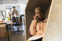 Femme d'affaires créative parlant sur le téléphone intelligent dans le cubby de bureau — Photo de stock