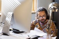Empresario creativo enfocado leyendo papeleo en la computadora en la oficina - foto de stock