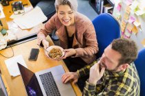 Gente creativa de negocios comiendo cereales, trabajando en la computadora portátil en la oficina - foto de stock