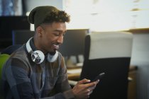 Empresário criativo sorridente com fones de ouvido usando telefone inteligente no escritório — Fotografia de Stock