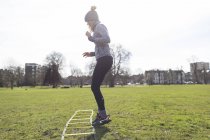 Femme pratiquant la vitesse perceuse échelle dans un parc ensoleillé — Photo de stock