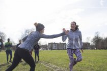 Women high-fiving, exercising in green park — Stock Photo