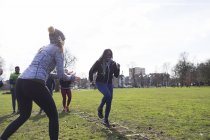 Woman cheering friend doing speed ladder drill in sunny park — Stock Photo