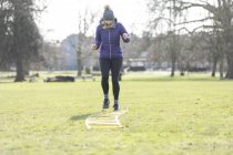 Woman doing speed ladder drill in sunny park — Stock Photo