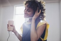 Усміхаючись, безтурботна молода жінка слухає музику з навушниками та mp3 плеєром — стокове фото