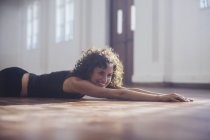 Smiling, carefree young female dancer stretching on dance studio floor — Stock Photo