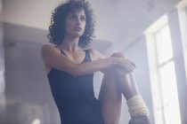 Зосереджена молода танцівниця розтягує ногу в танцювальній студії — стокове фото