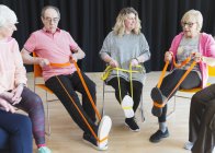 Active seniors exercising in circle, using straps to stretch legs — Stock Photo