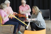 Ausbilder hilft aktiven Senioren, Beine zu strecken, mit Gurten zu trainieren — Stockfoto