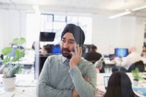 Serious Indian businessman in turban talking on smart phone in office — Stock Photo