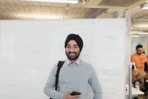 Retrato sonriente, empresario indio confiado en turbante parado en pizarra en la oficina - foto de stock
