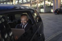 Homme d'affaires souriant utilisant un ordinateur portable dans un taxi crowdsourced la nuit — Photo de stock