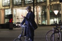 Бізнесмен з смарт-телефону та велосипед на міські вулиці вночі — стокове фото