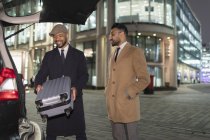 Uomini d'affari che caricano valigia in auto all'angolo della strada urbana di notte — Foto stock