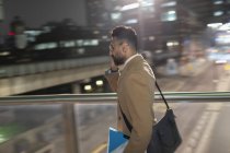 Businessman talking on smart phone, walking on urban pedestrian bridge at night — Stock Photo