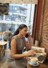 Femme d'affaires parlant sur le téléphone intelligent, travaillant à un ordinateur portable dans un café — Photo de stock