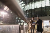 Бизнесмены с чемоданом обсуждают документы на городской пешеходный мост ночью — стоковое фото
