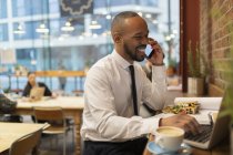 Улыбающийся бизнесмен разговаривает по смартфону, работает в кафе — стоковое фото