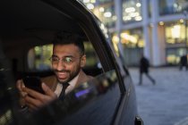 Businessman using smart phone in crowdsourced taxi at night — Stock Photo