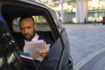 Empresário lendo papelada em táxi crowdsourced à noite — Fotografia de Stock