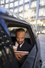 Businessman drinking coffee, using digital tablet in crowdsourced taxi — Stock Photo