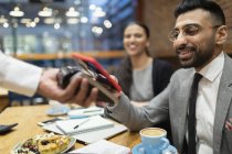 Uomo d'affari che paga con smart phone pagamento contactless in caffè — Foto stock