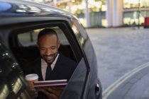 Businessman drinking coffee and using digital tablet in crowdsourced taxi — Stock Photo