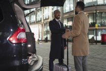 Businessmen with suitcase handshaking at back of car on urban street at night — Stock Photo