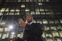 Businessman using smart phone below urban highrise at night — Stock Photo