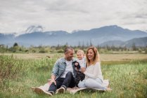 Parents and baby son sitting in rural field with mountains in background — Stock Photo