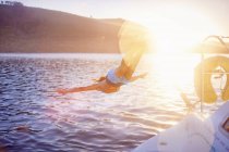 Женщина, прыгающая с лодки в солнечный океан — стоковое фото