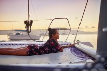 Serene young woman relaxing on catamaran net at sunset — Stock Photo