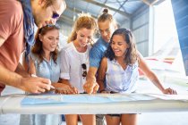 Friends planning trip at map in airplane hangar — Stock Photo