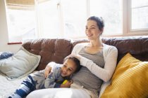 Ласковая мать и маленький сын обнимаются на диване в гостиной — стоковое фото