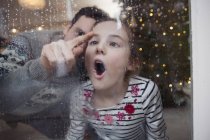 Playful father and daughter drawing in condensation on wet winter window — Stock Photo