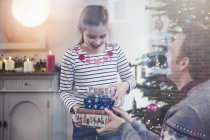 Tochter übergibt Stapel Weihnachtsgeschenke an Vater im Wohnzimmer — Stockfoto