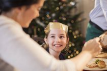 Усміхнена дівчина в паперовій короні насолоджується різдвяною вечерею — стокове фото