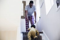 Батько в піжамі дивиться, як маленький син повзе по сходах — стокове фото