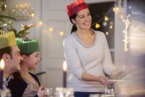 Happy mother in paper crown serving Christmas pudding with fireworks at candlelight table — Stock Photo