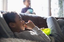 Хлопчик їсть закуску і дивиться телевізор на дивані — стокове фото
