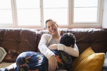 Счастливая, беззаботная мать обнимается с сыном на диване в гостиной — стоковое фото
