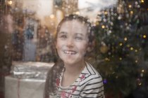 Portrait happy girl at wet window in Christmas living room — Stock Photo