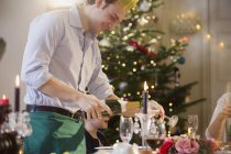 Sonriente hombre vertiendo champán en la cena de Navidad a la luz de las velas - foto de stock