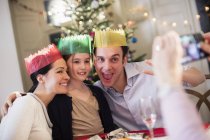 Playful family in paper crowns posing for photograph at Christmas dinner table — Stock Photo